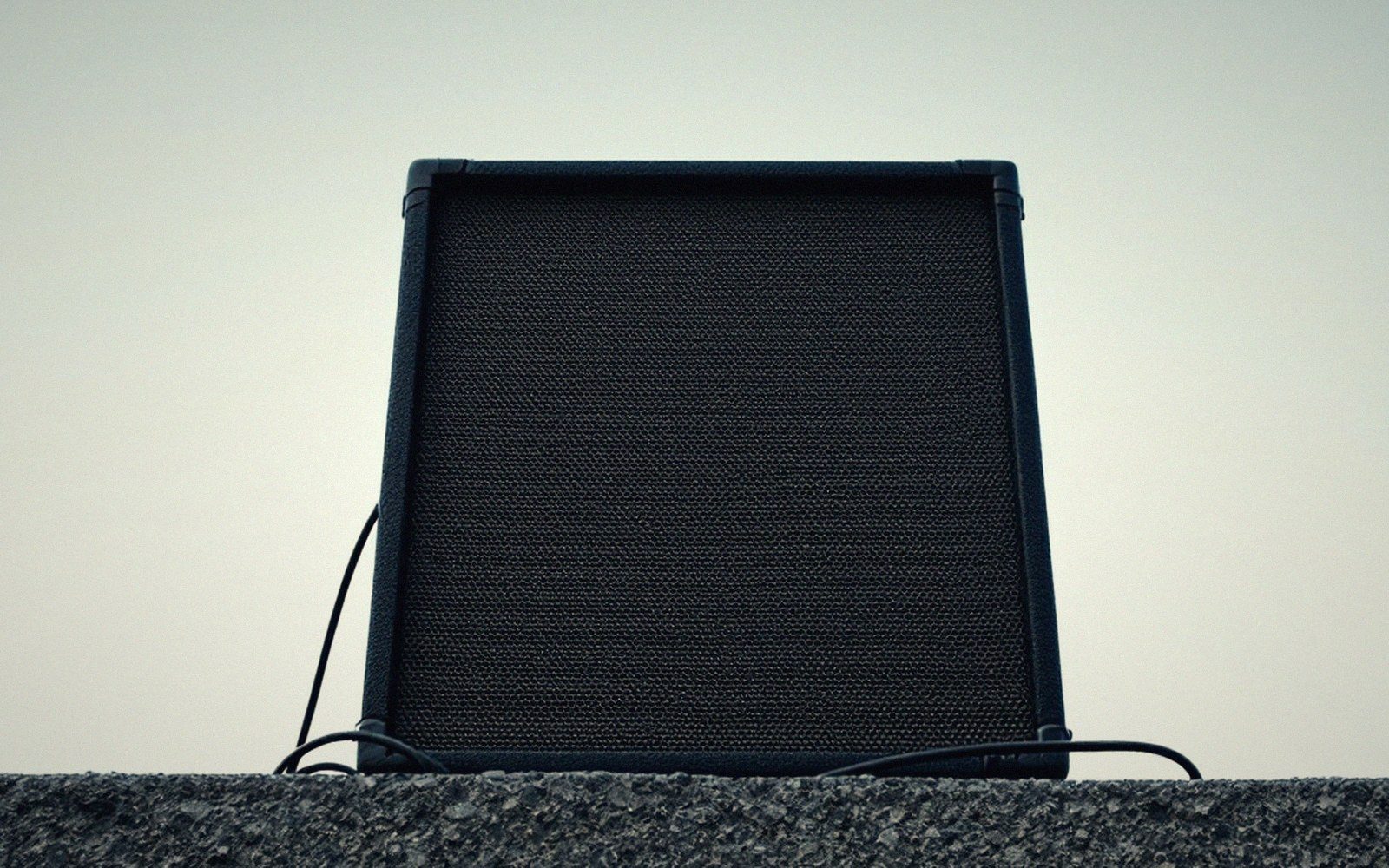 Detail of a single large speaker cabinet, grille cloth and porting visible, shot from below against a plain sky